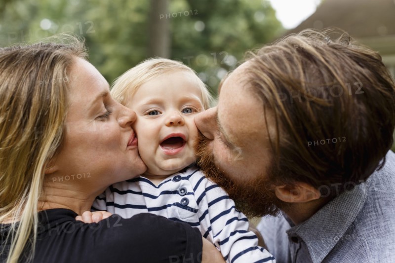 Mother and father kissing baby girl on cheek