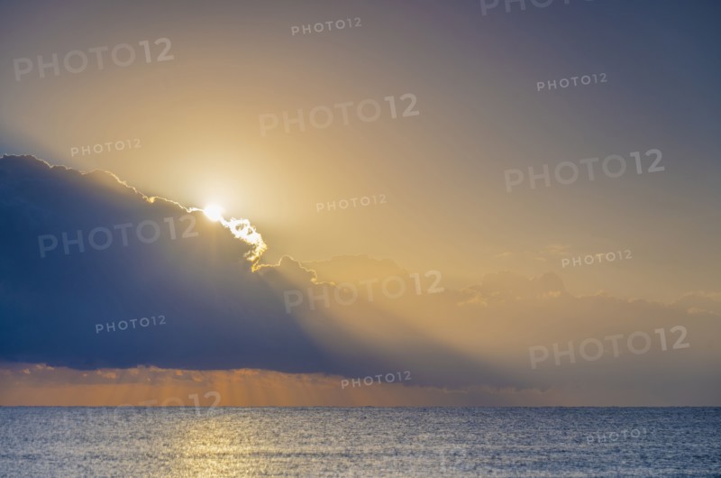 Sun rising behind clouds above sea