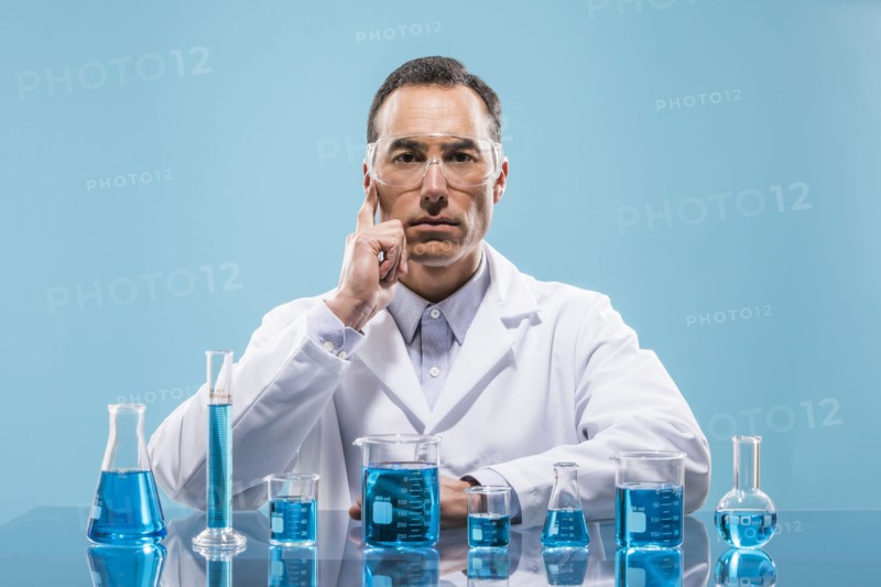 Portrait of scientist with beakers with blue liquid in foreground