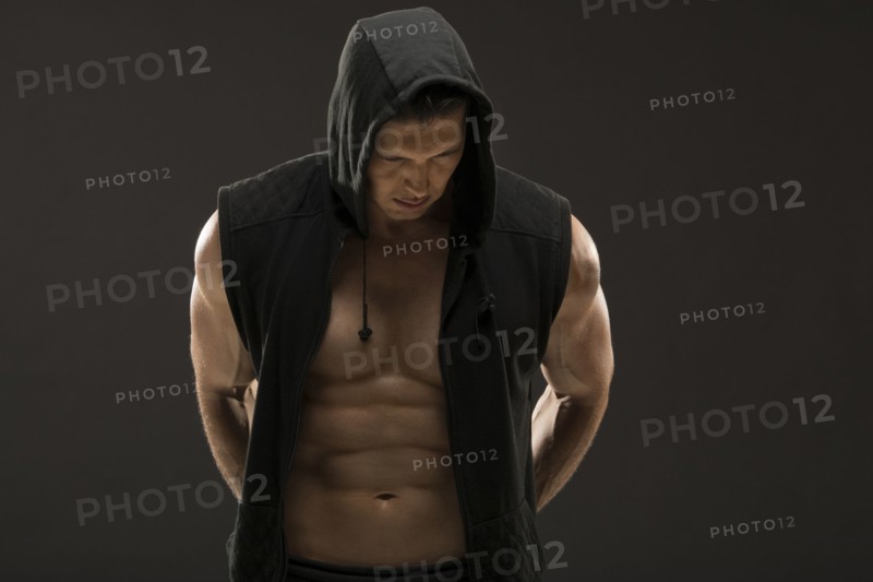 Muscular man in hooded vest against black background