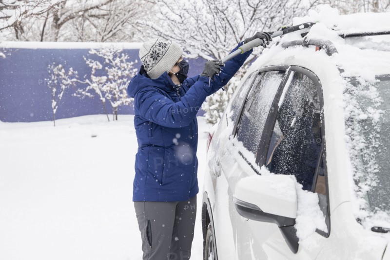 Woman in face mask removing snow from car
