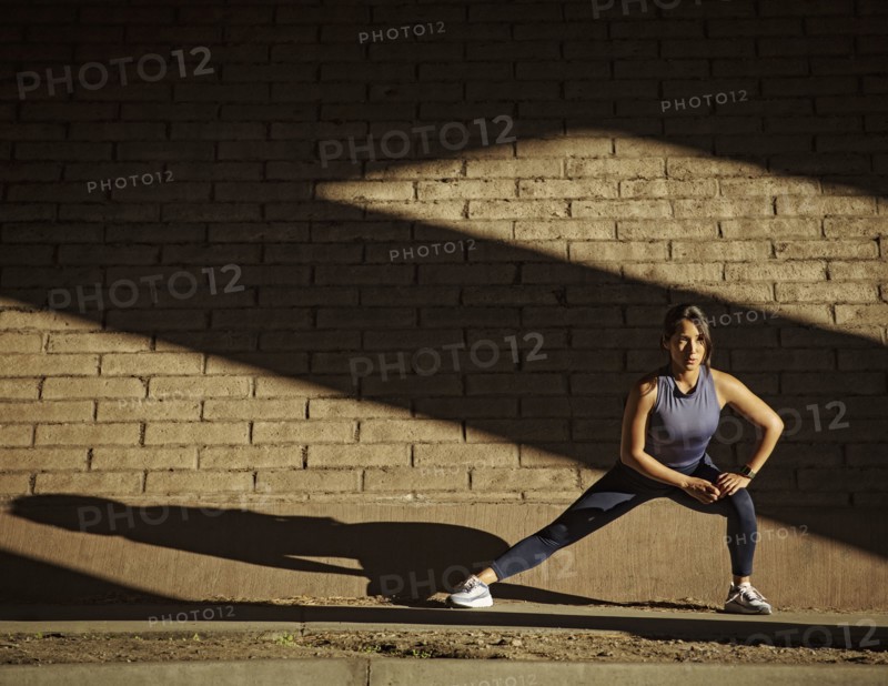 Woman stretching near brick wall in sunlight