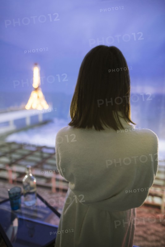 Rear view of woman in bathrobe in hotel with view on sea at night