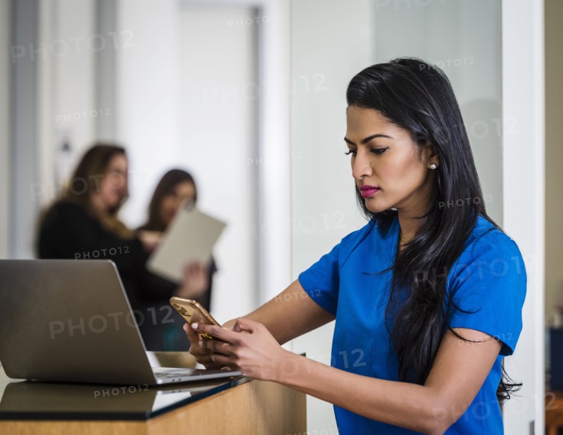 Female doctor with smart phone and laptop at reception desk