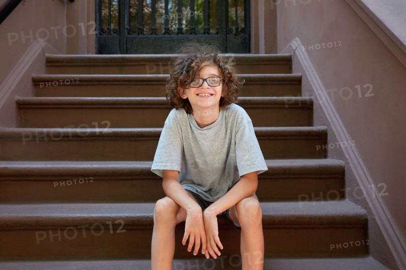 USA, New York, New York City, Boy sitting on steps in front of building