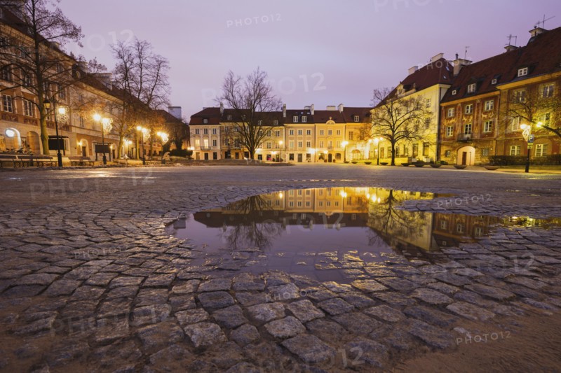 Poland, Masovia, Warsaw, Illuminated town square reflecting in puddle at night