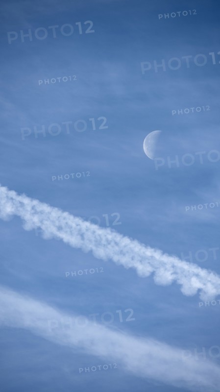 Airplane contrails and waning moon against blue sky