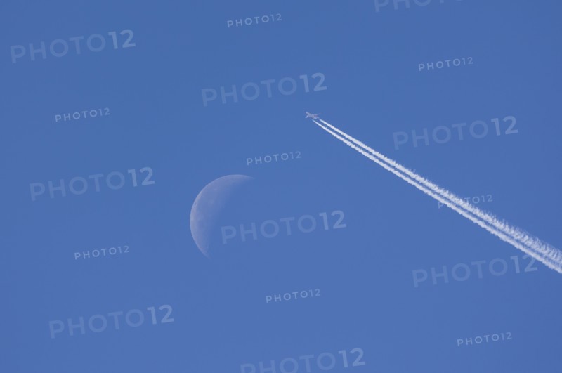 Airplane leaving contrails against blue sky with waning moon