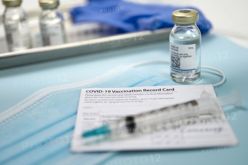 Syringe on Covid-19 vaccination record card and vials on tray