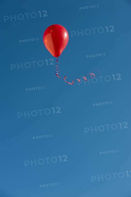 Red balloon with ribbon flying against blue sky