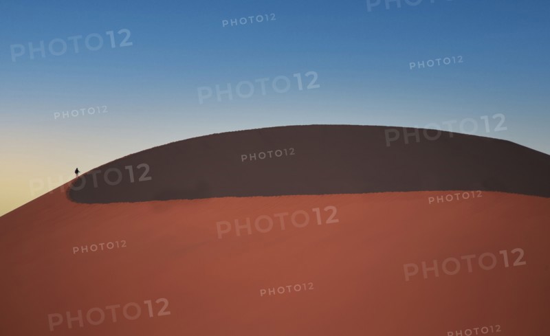 Lone man climbing giant sand dune