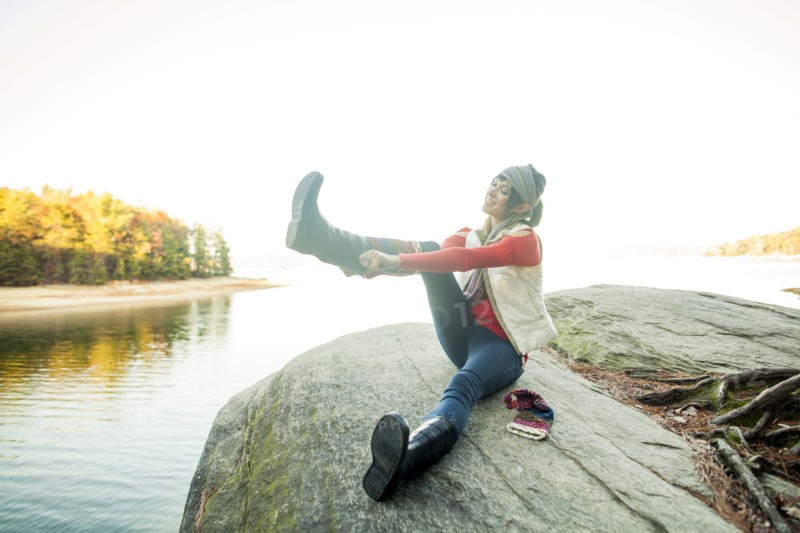 Caucasian woman pulling on boots near lake