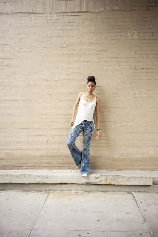 Serious African American woman standing on ledge at brick wall