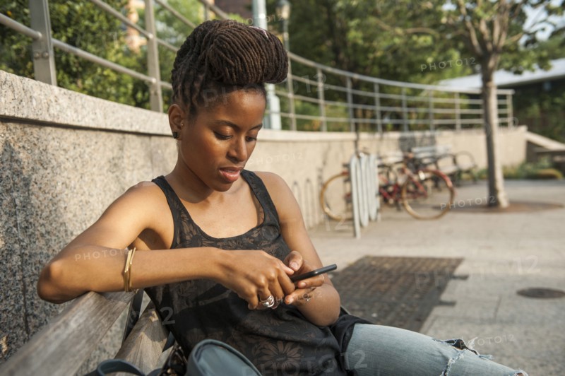 African American woman on bench at park texting on cell phone