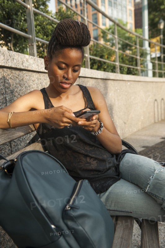 African American woman on bench at park texting on cell phone