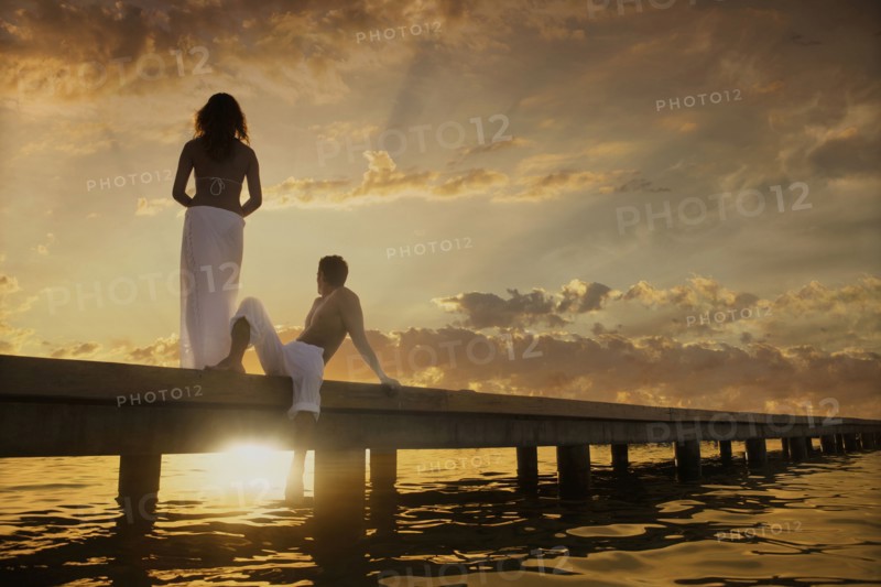 Caucasian couple admiring sunset from dock over ocean