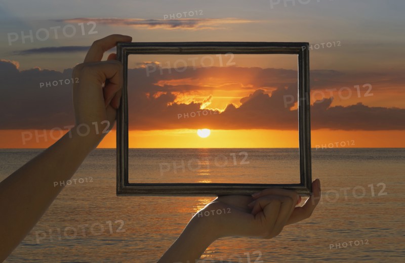 Caucasian woman holding frame over dramatic sunset sky and ocean