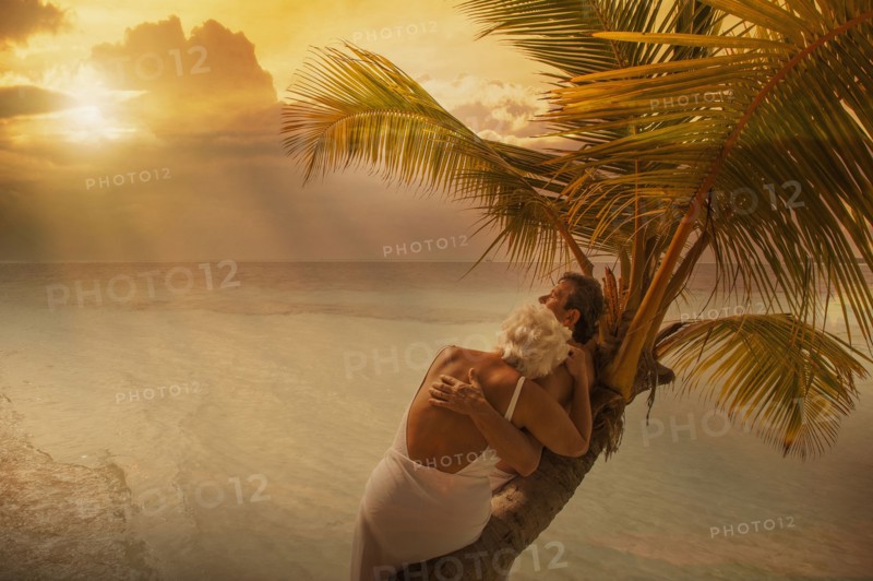 Older Caucasian couple hugging on palm tree at beach