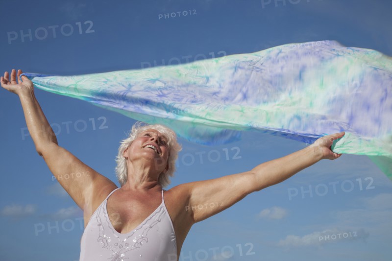 Older Caucasian woman holding fabric in wind under blue sky