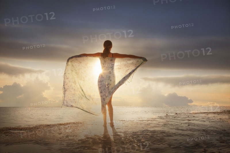 Caucasian woman holding fabric on beach at sunset