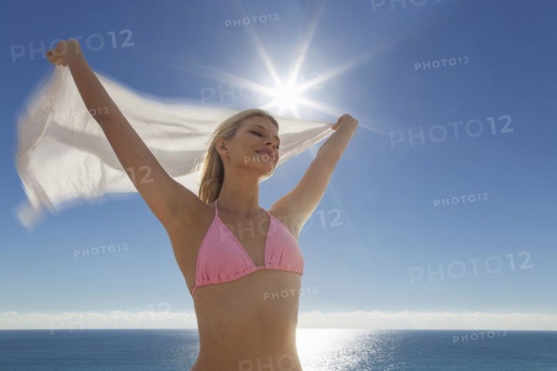 Caucasian woman in bikini holding fabric at beach