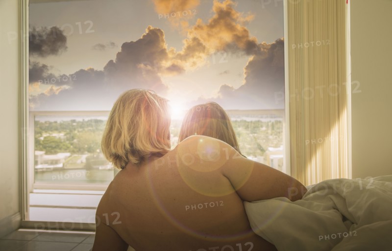 Caucasian couple in bed watching sunset at window