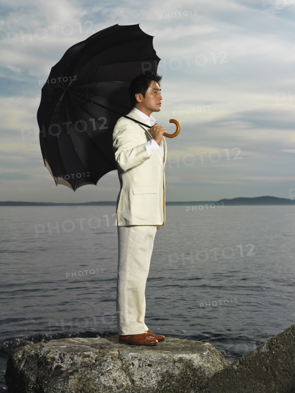 Japanese businessman holding umbrella near ocean