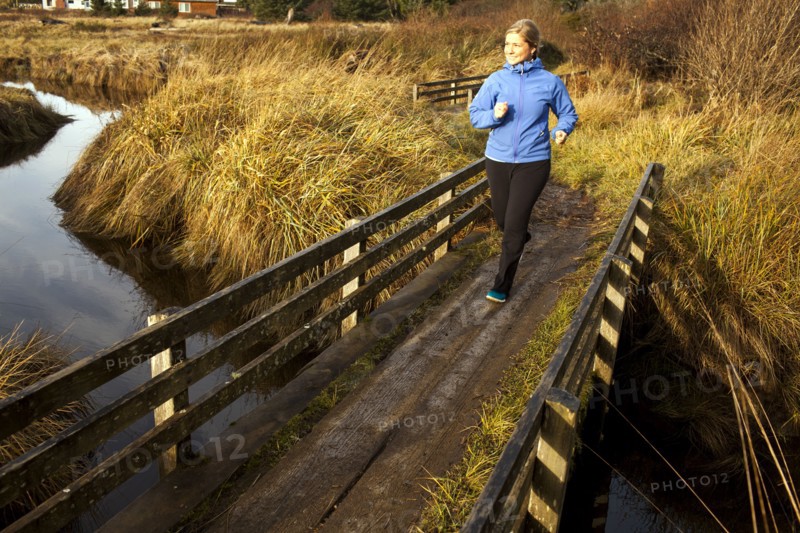 Caucasian woman jogging on wood bridge over creek
