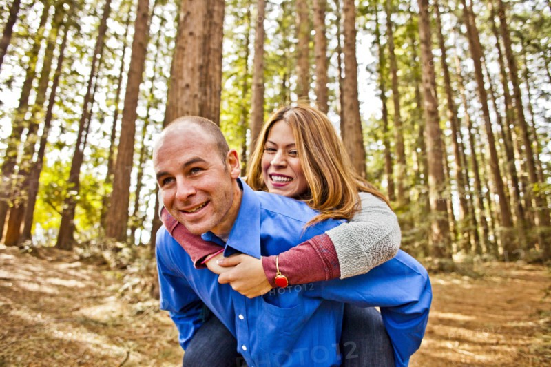 Hispanic man carrying girlfriend piggy back in forest