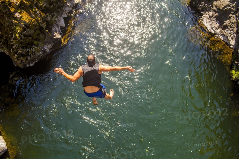 Caucasian man jumping off rocks into ocean