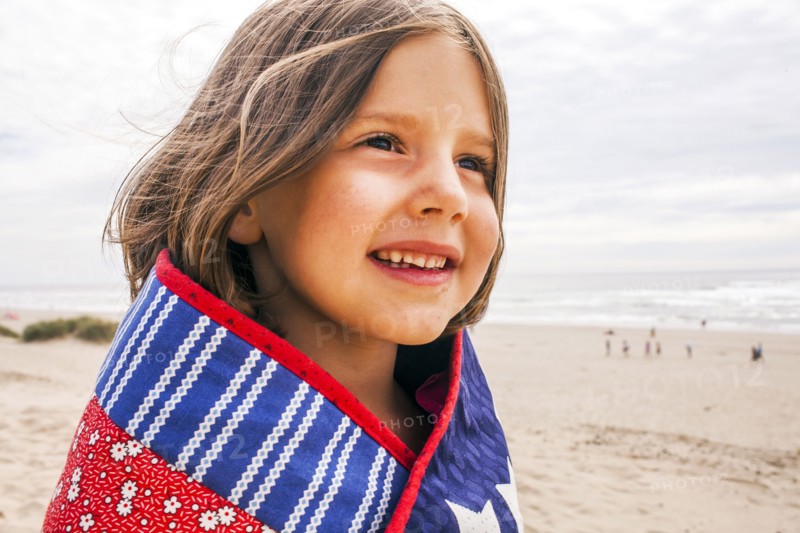 Caucasian girl wrapped in blanket on beach