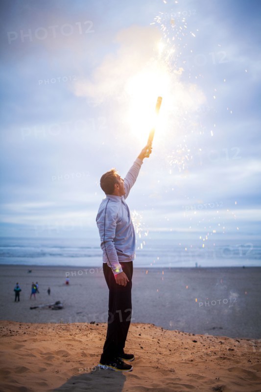 Caucasian man holding fireworks on beach