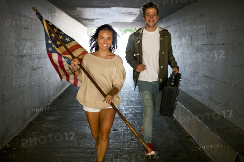 Caucasian couple carrying American flag and boom box in tunnel