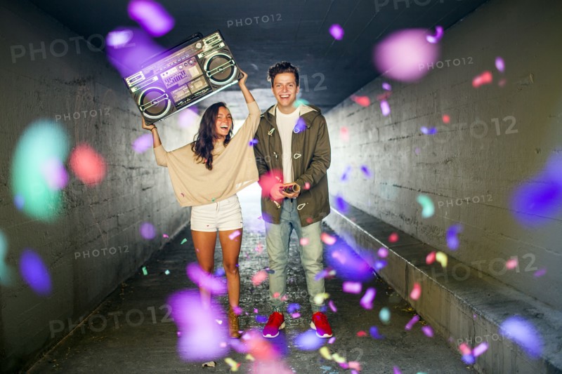 Caucasian couple carrying boom box and throwing confetti in tunnel