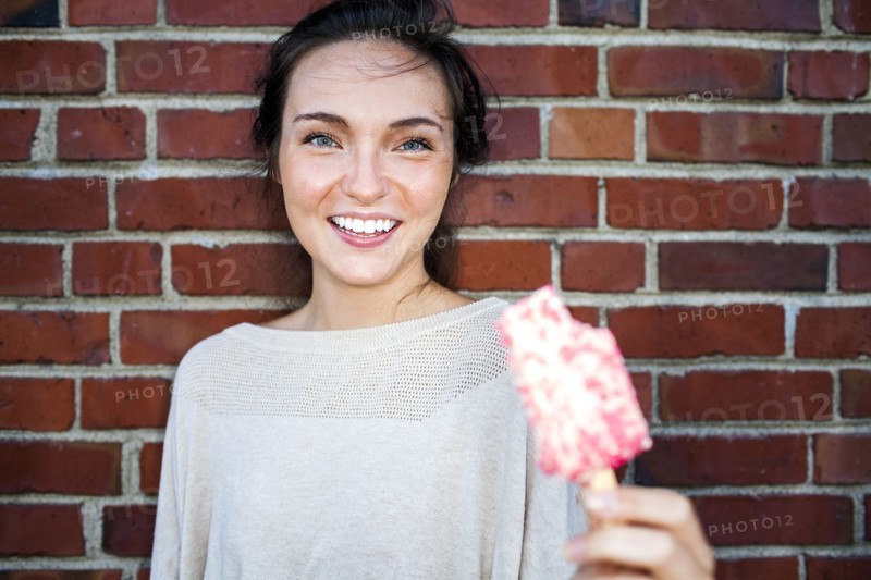 Caucasian woman eating ice cream near red brick wall