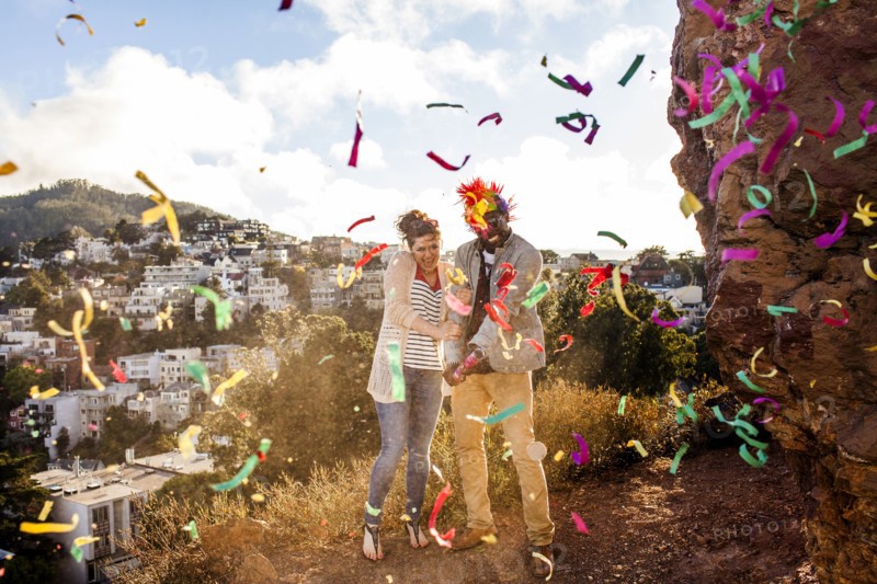 Couple throwing confetti on hill overlooking cityscape