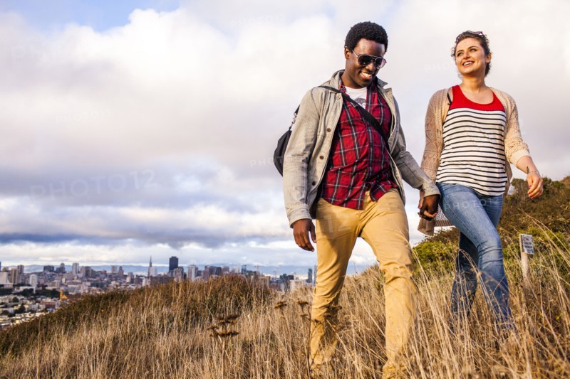 Couple walking on grassy hill overlooking cityscape