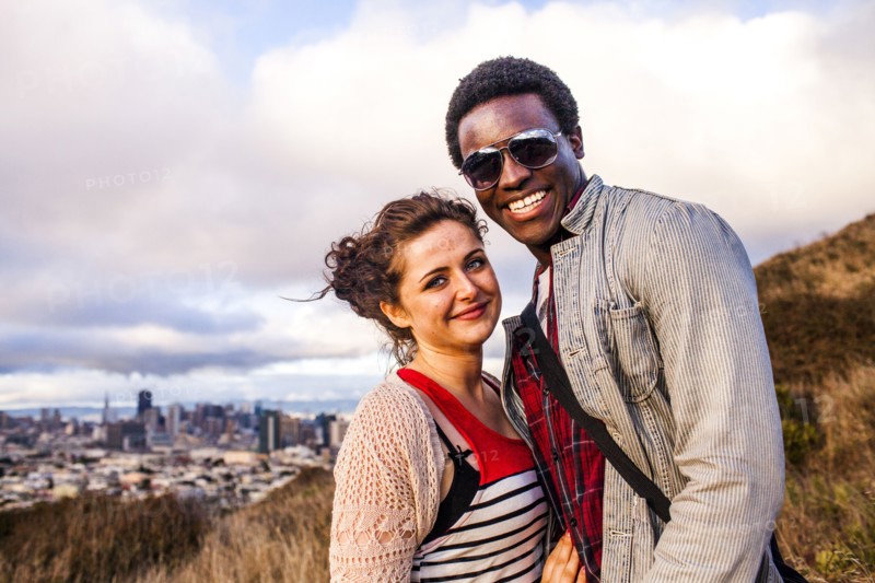 Couple smiling on grassy hill overlooking cityscape