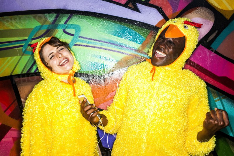 Couple in identical costumes listening to earbuds near graffiti wall