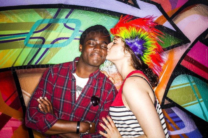 Woman in colorful wig kissing boyfriend near graffiti wall