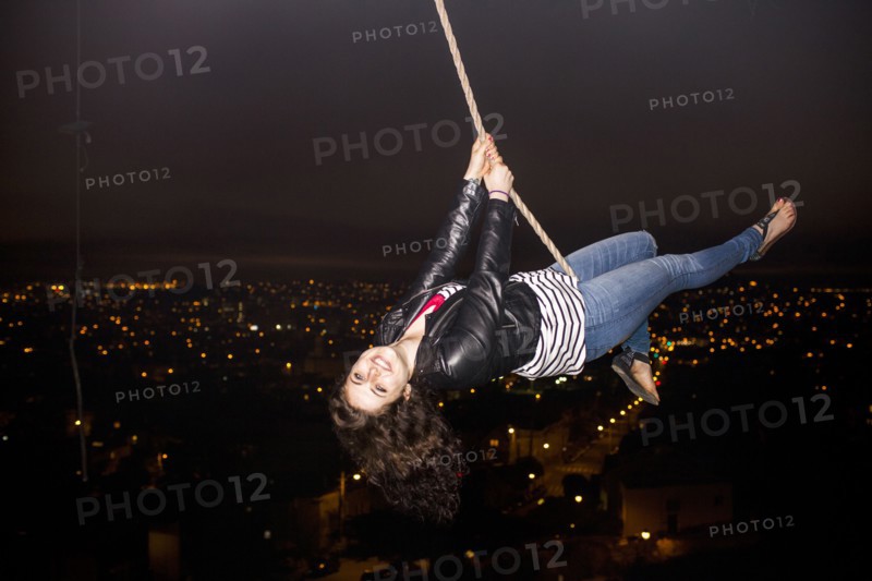 Caucasian woman on rope swinging over scenic view of cityscape