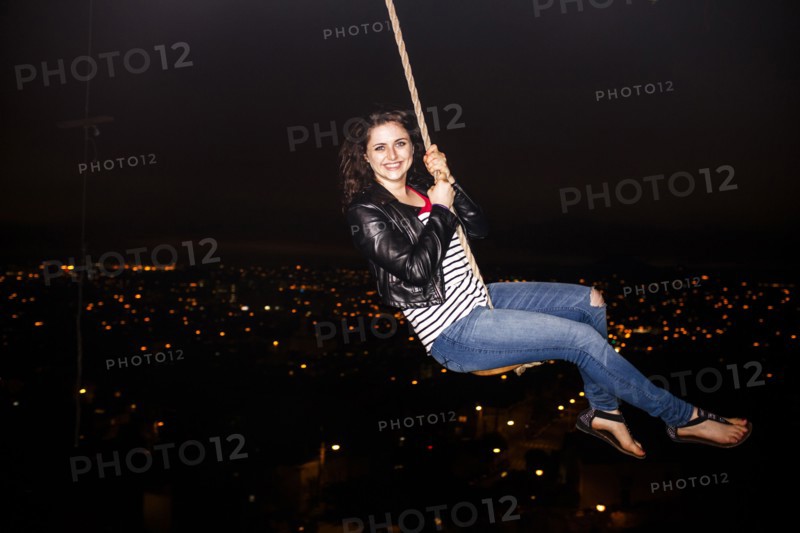 Caucasian woman on rope swinging over scenic view of cityscape