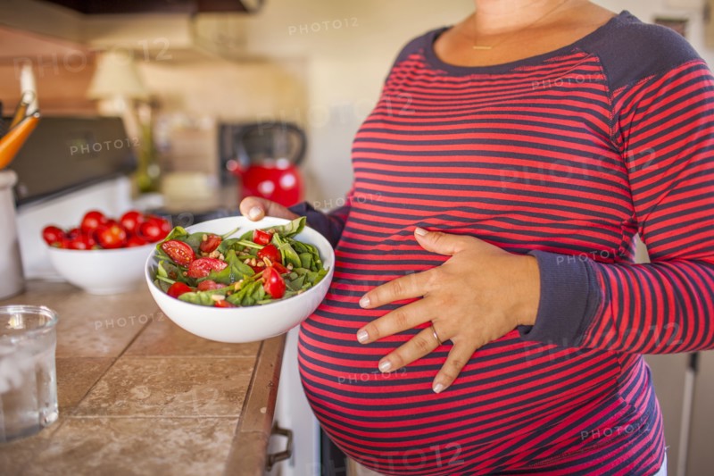 Pregnant Caucasian mother holding salad in kitchen