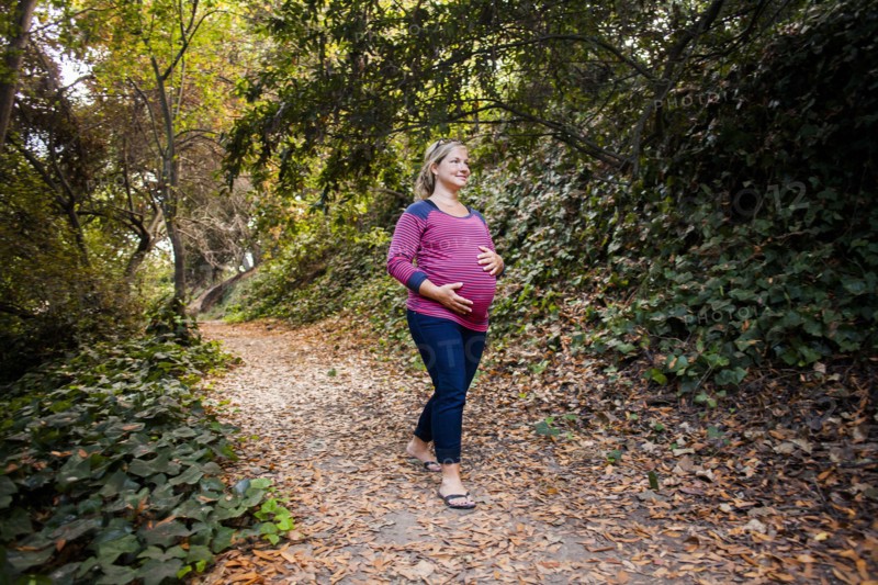 Pregnant Caucasian woman holding her stomach on forest path