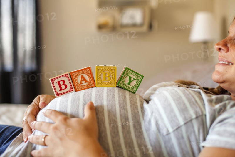 Pregnant Caucasian woman balancing wooden blocks on her stomach in bed