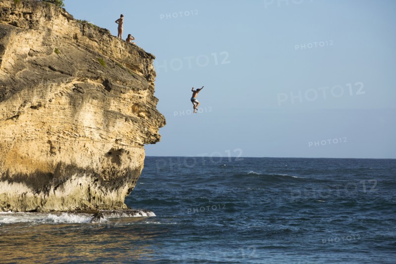 Divers jumping off cliff into ocean