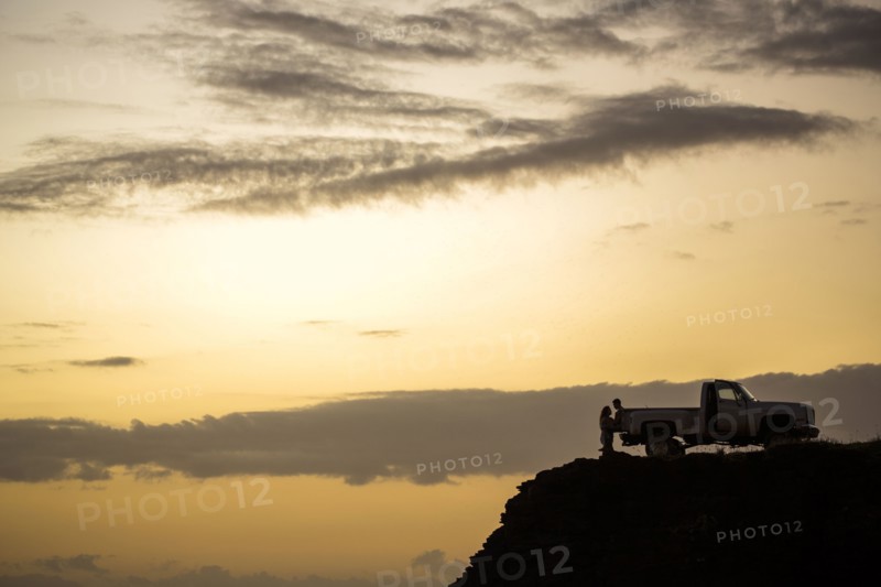 Silhouette of people sitting on pickup truck on cliff at sunset