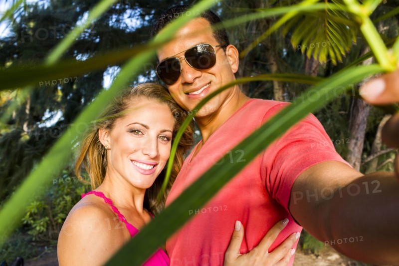 Smiling couple hugging behind palm frond leaves