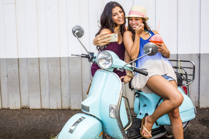 Pacific Islander women taking cell phone photograph on scooter