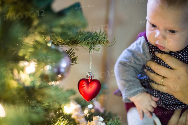 Caucasian parent holding baby girl near Christmas tree